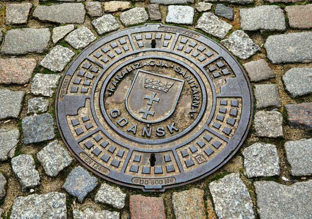 Circular Gdańsk manhole cover set in cobblestone street, showcasing urban infrastructure.